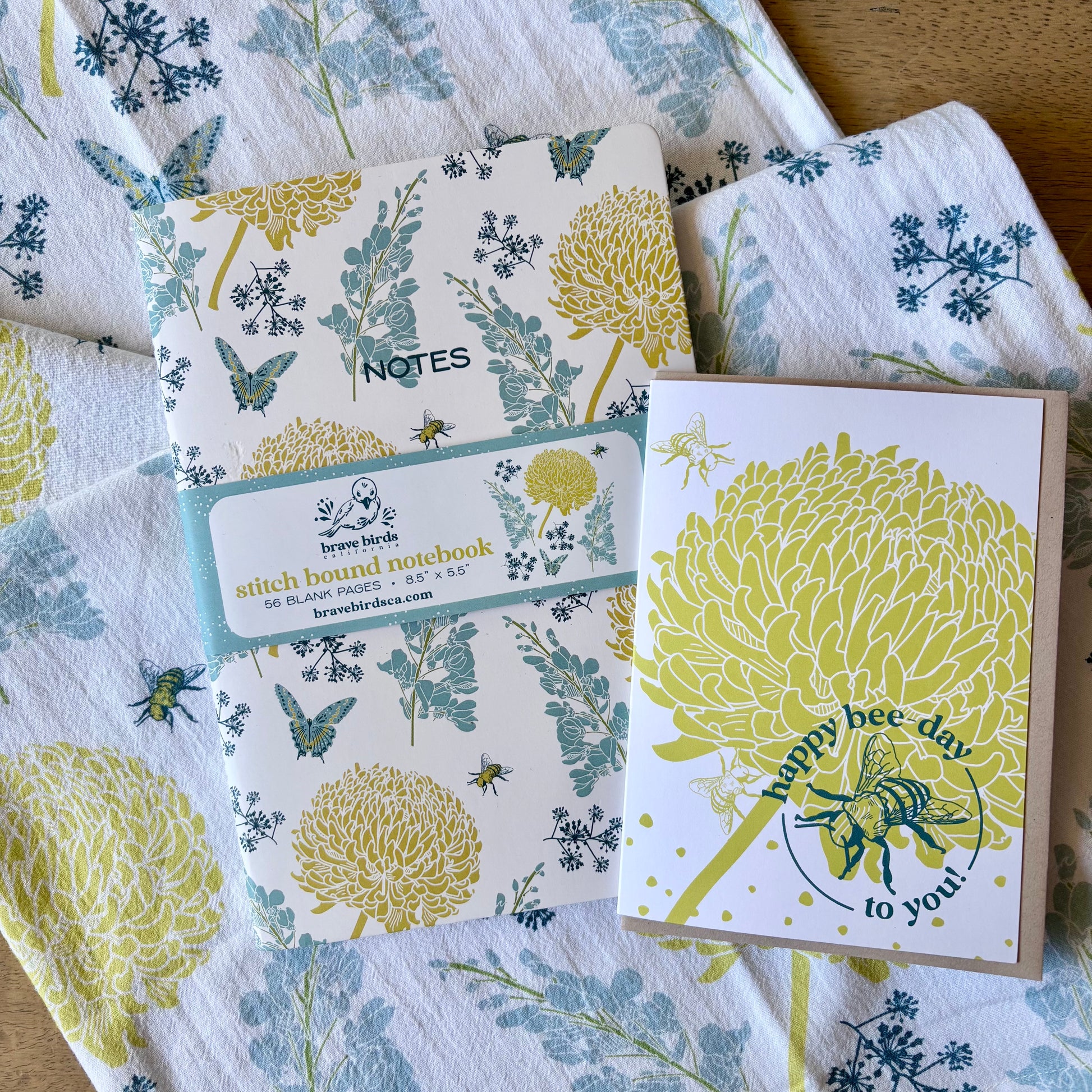 Notebook and card with floral and bee design on a matching patterned tea towel