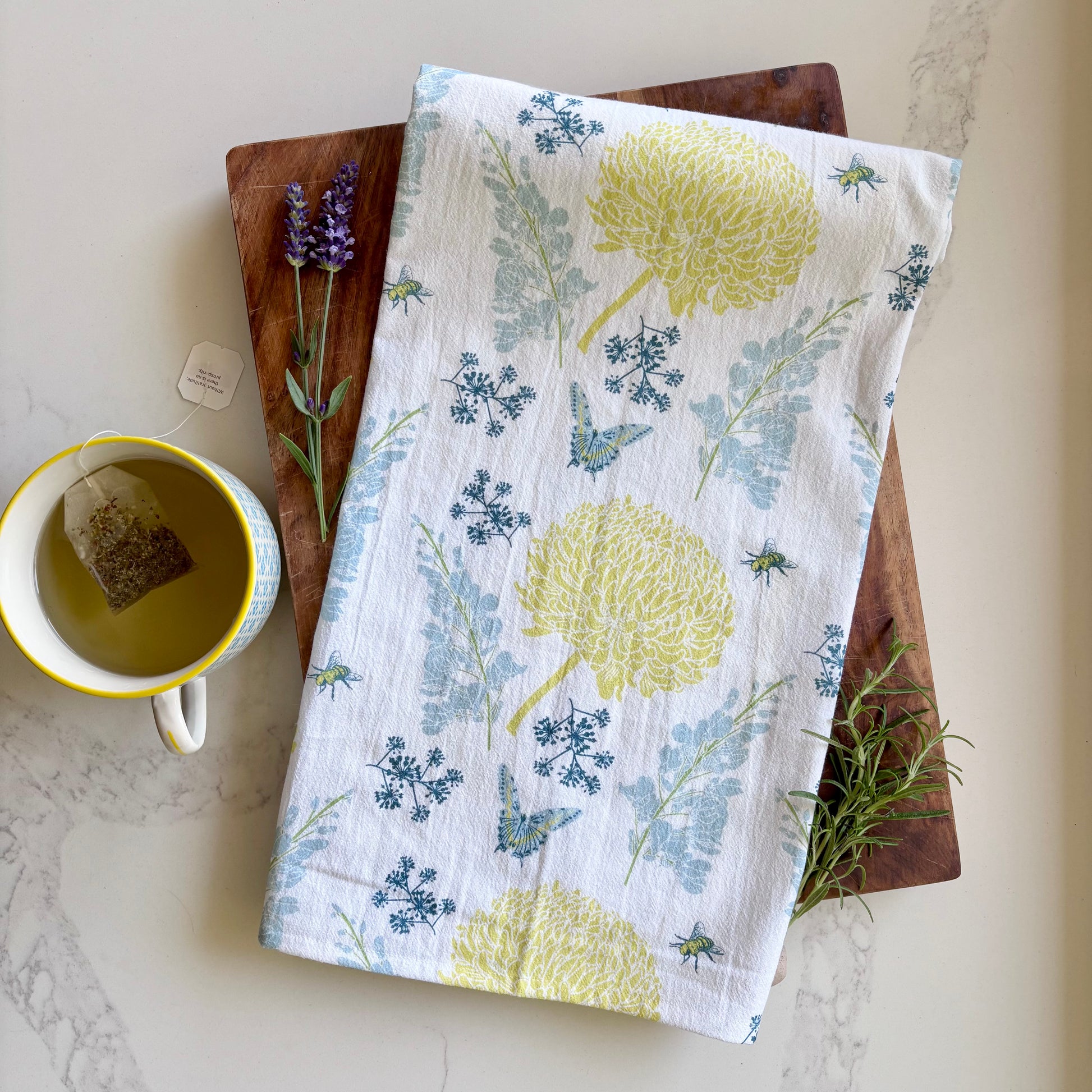 Blue and yellow floral print tea towel shown with fresh herbs and a cup of tea