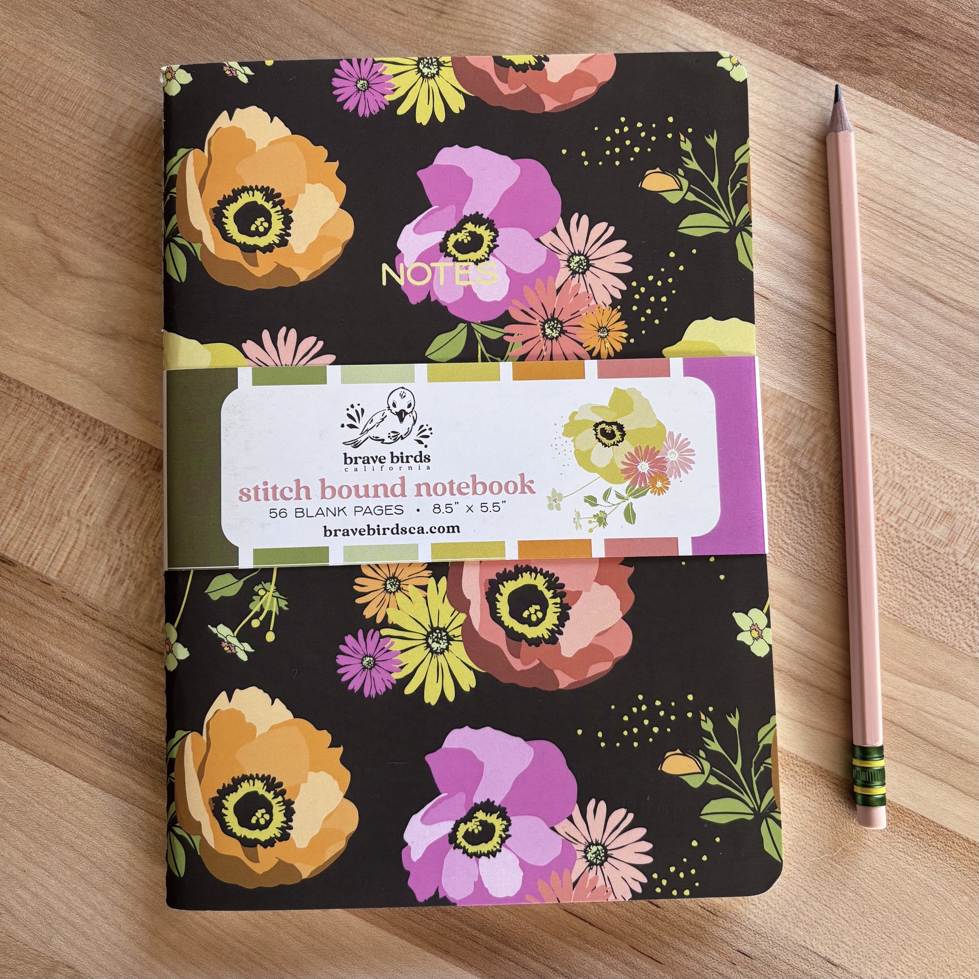Brown, purple and orange floral print notebook shown on a wood table with a pencil