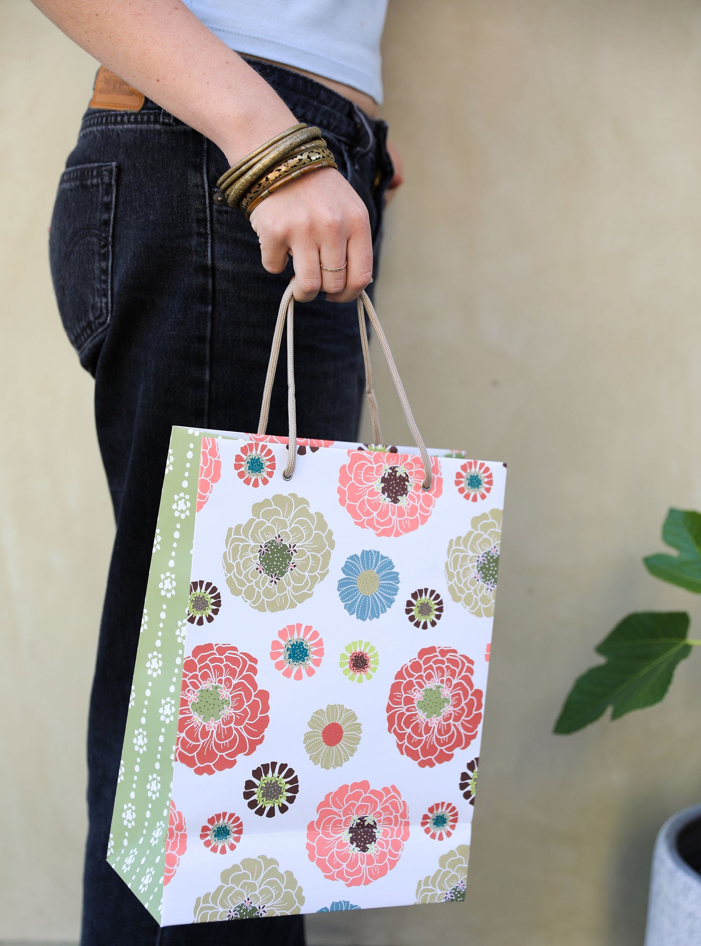 Woman in jeans holding a gift back with a colorful floral print on the front and a subtle green grounded dot print on the side panel