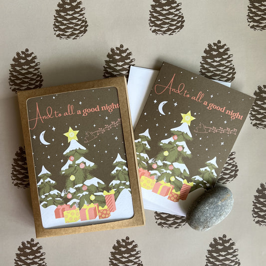 Holiday cards with a nighttime forest scene, decorated tree and Santa sleigh silhouette flying in the starry sky. Text reads "And to all a good night" and the photo shows a boxed set as well as a single card and envelope.