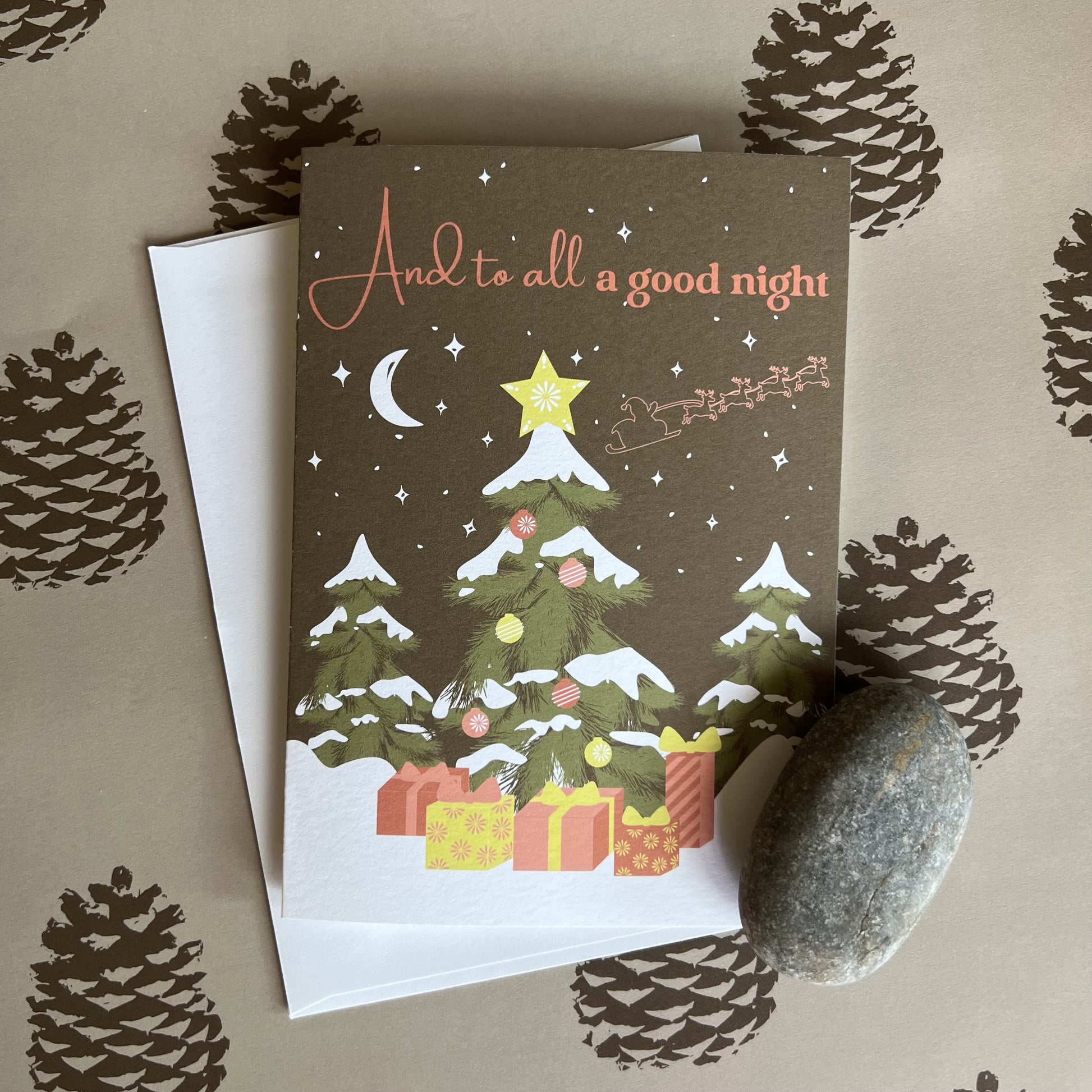 Holiday card with a nighttime forest scene, decorated tree and Santa sleigh silhouette flying in the starry sky. Text reads "And to all a good night" and the photo shows a single card and envelope.