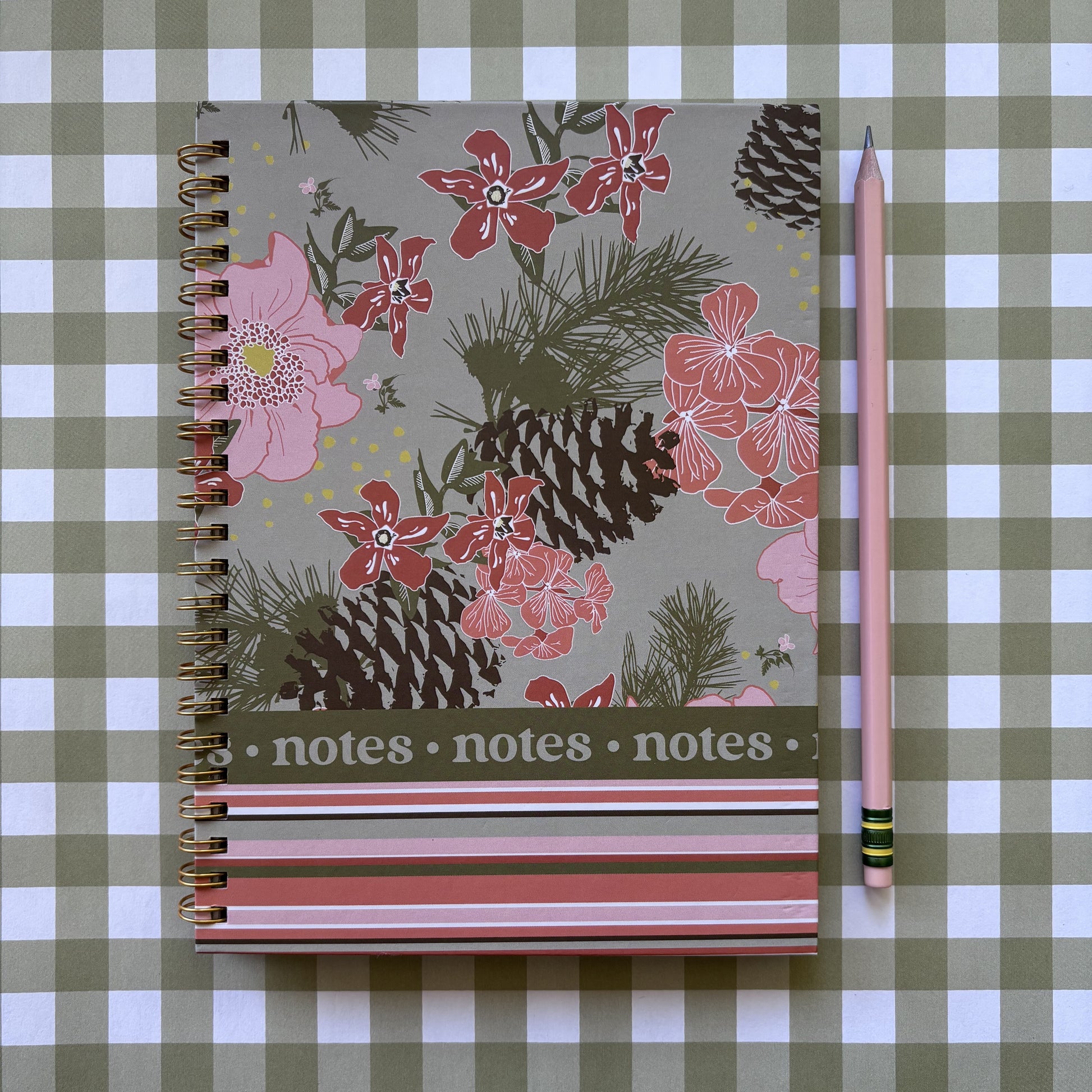 pink and green floral and stripe spiral notebook with pinecones on green and white plaid background with pink pencil