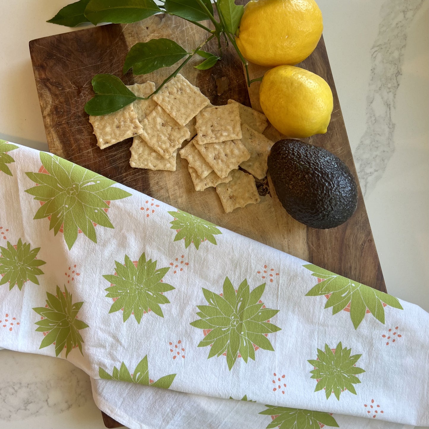 Succulent tea towel styled with a wood board, lemons, avocado and crackers