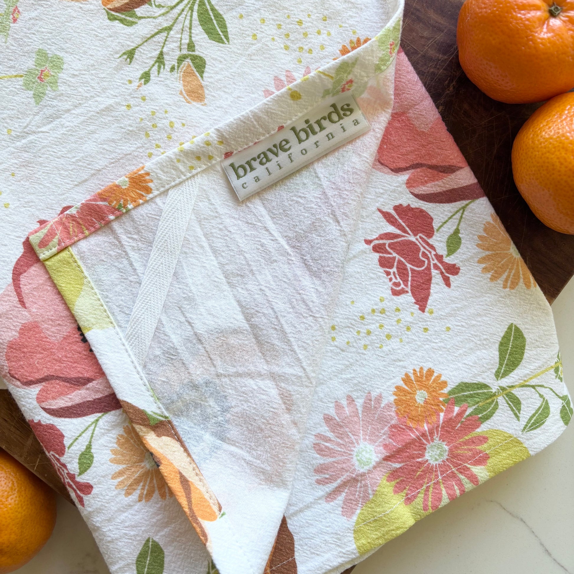 Floral-patterned cloth with a brand label next to oranges on a wooden surface