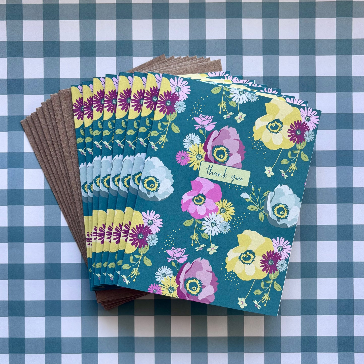 Fanned stack of thank you greeting cards with bright floral print and kraft brown envelopes