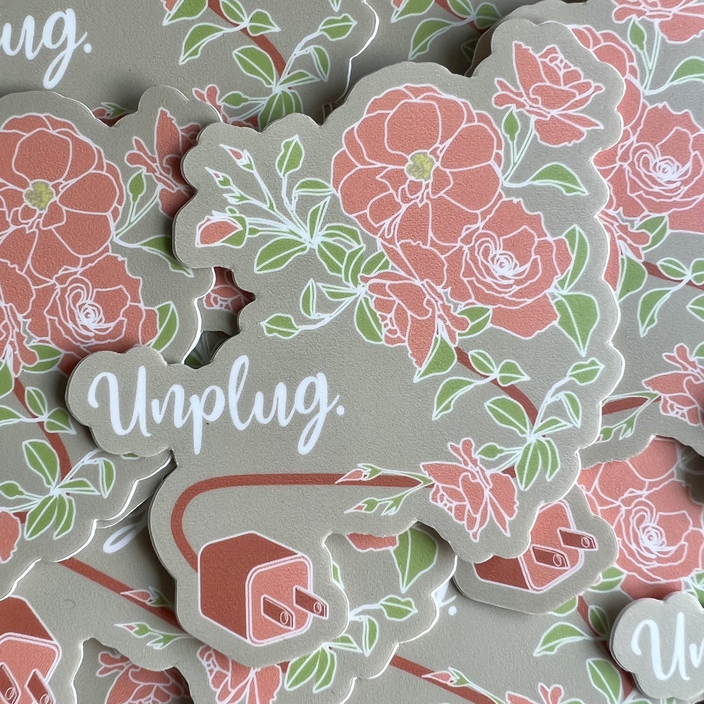 Khaki background sticker with a pink plug and a cord that turns into a stem for blossoming roses. Text reads "Unplug".