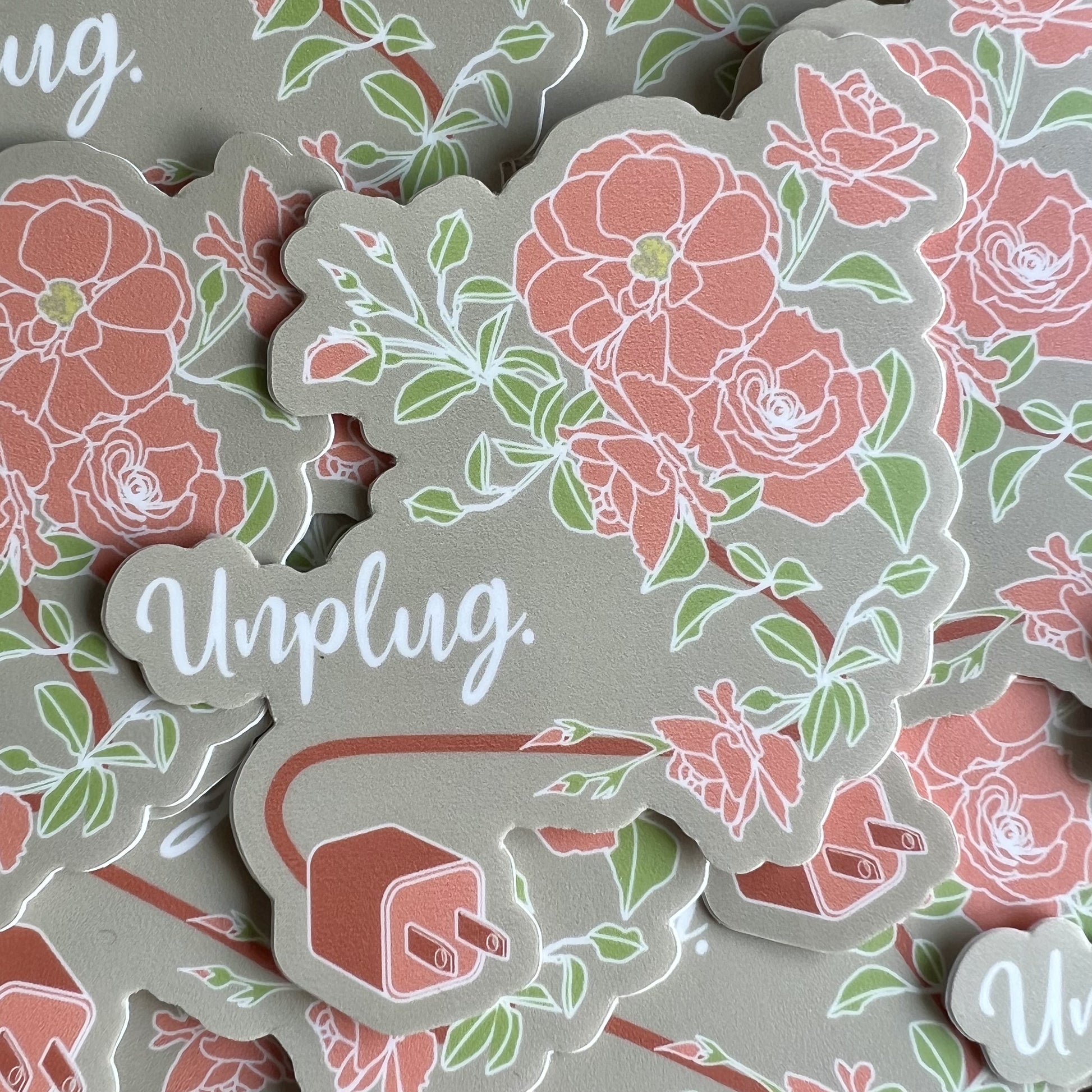 Khaki background sticker with a pink plug and a cord that turns into a stem for blossoming roses. Text reads "Unplug".