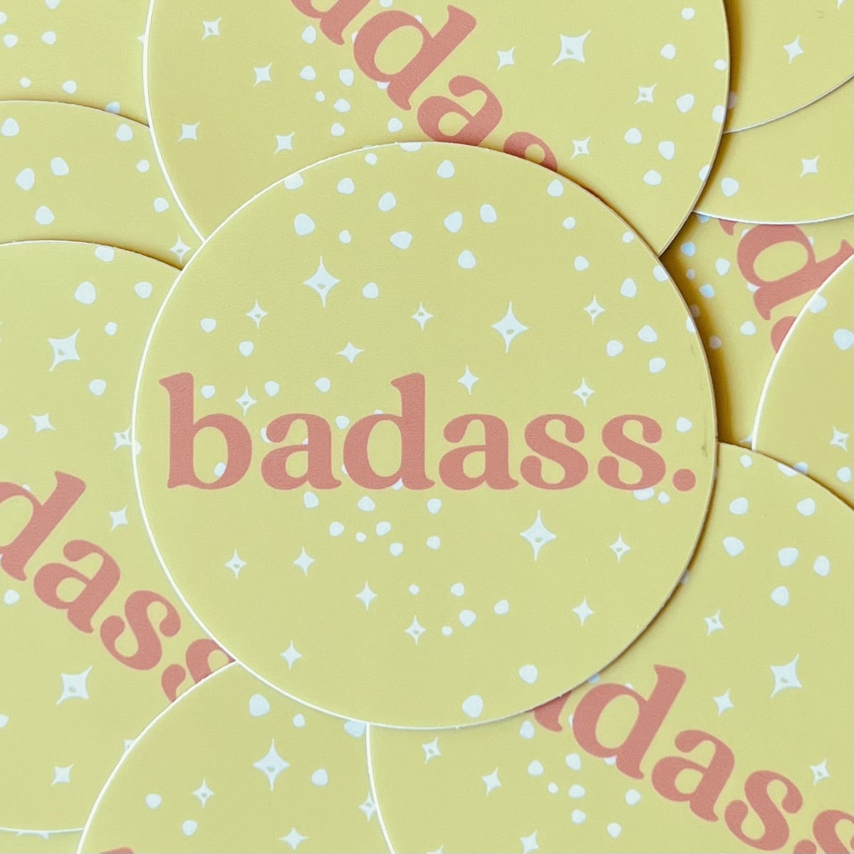 Yellow round sticker with white spots & stars and the word badass in dark pink ink