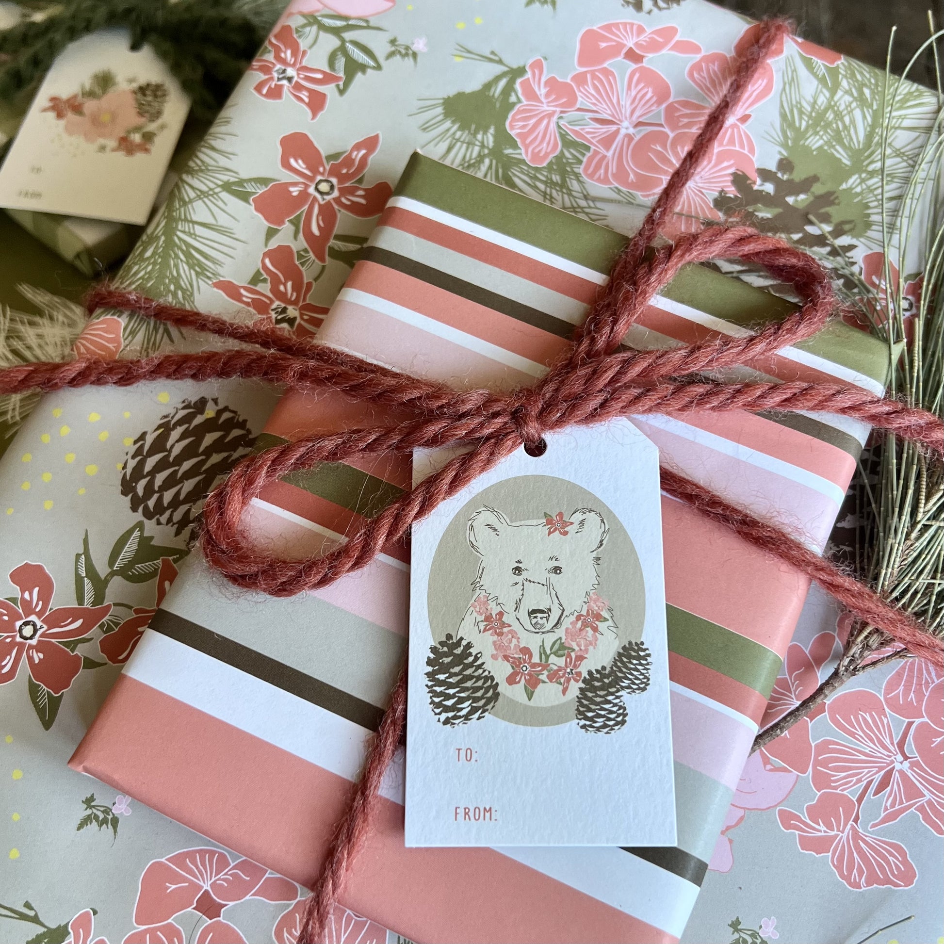 Gift wrapped package tied with red yarn and a TO/FROM gift tag with an illustration of a bear with flower necklace and a flower in her ear.