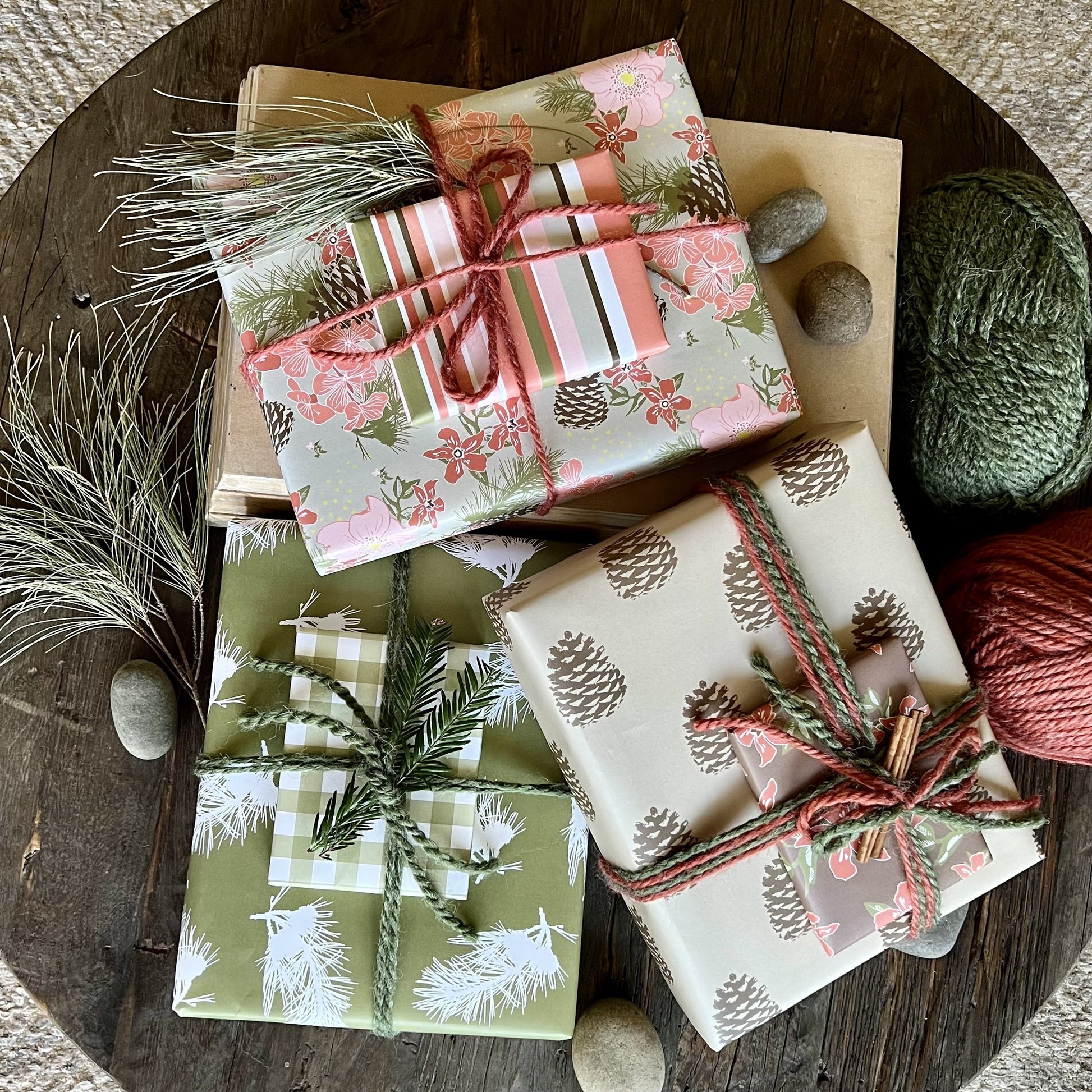 Pile of three giftwrapped boxes in pine branch and pinecone patterns, in pink, olive and brown color palette and tied with yarn