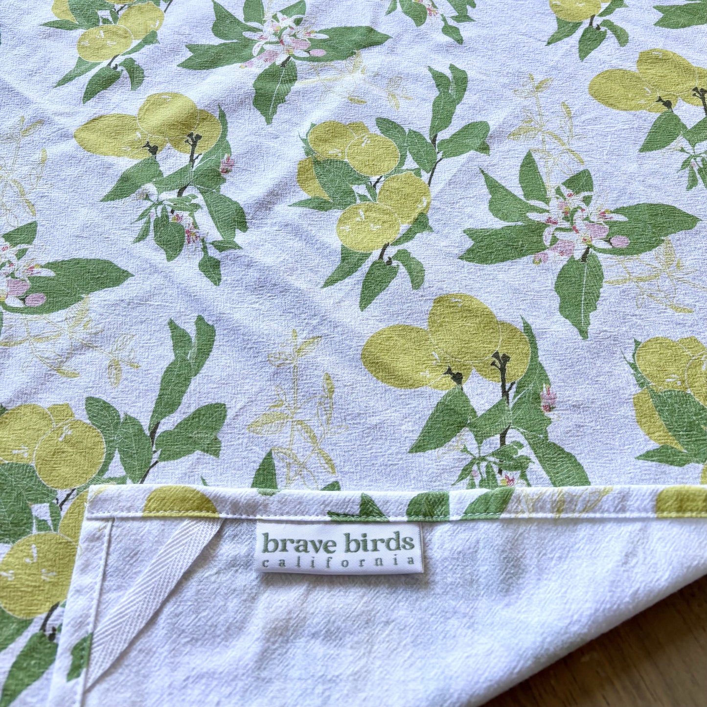 Flat detail shot of lemon print tera towel with corner foled to show hanging loop and sewn-in logo label
