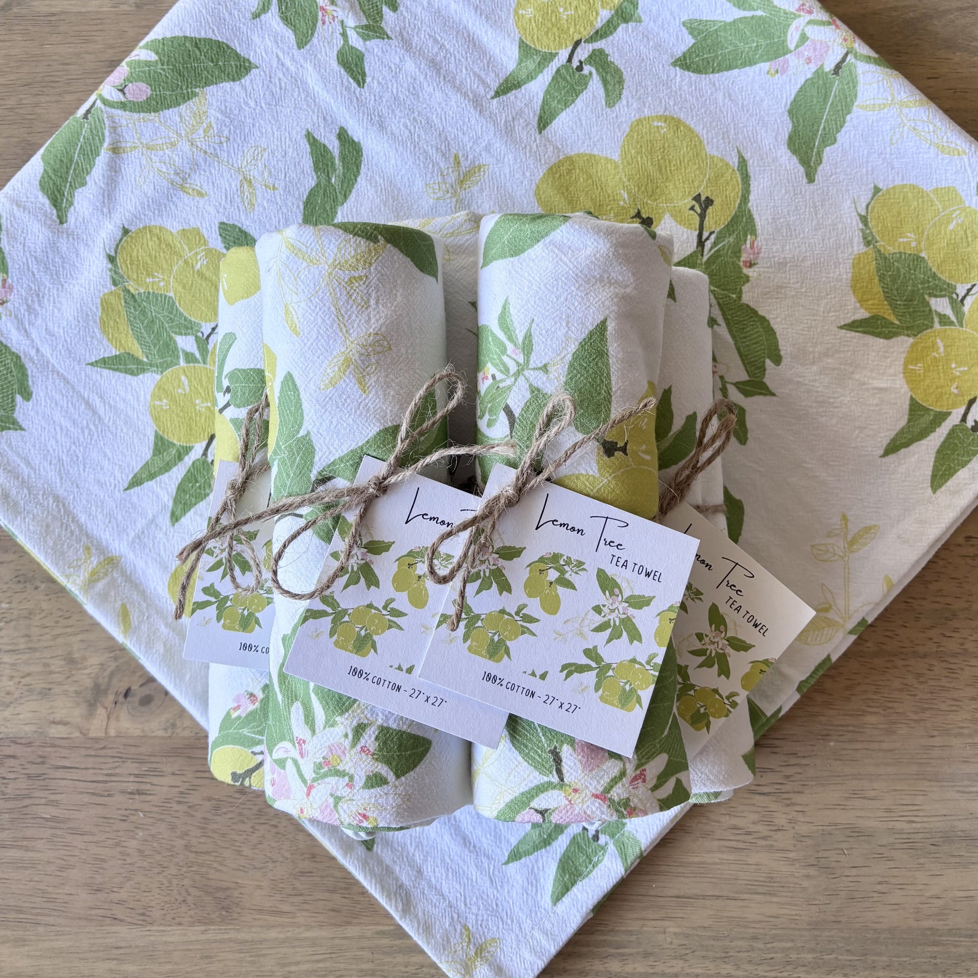 Stacked of rolled up lemon print tea towels, tied with twine and square printed hang tags