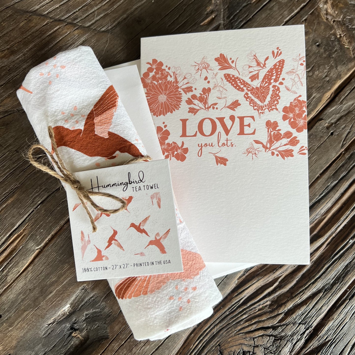 hummingbird tea towel and butterfly garden greeting card, both with white backgrounds and dark pink illustrations