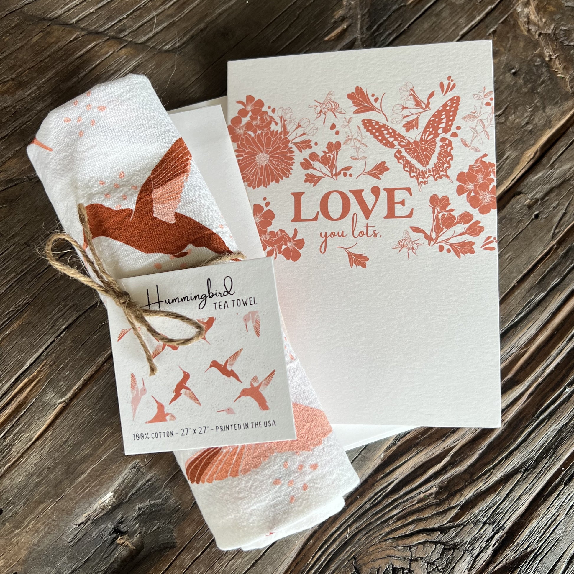 hummingbird tea towel and butterfly garden greeting card, both with white backgrounds and dark pink illustrations