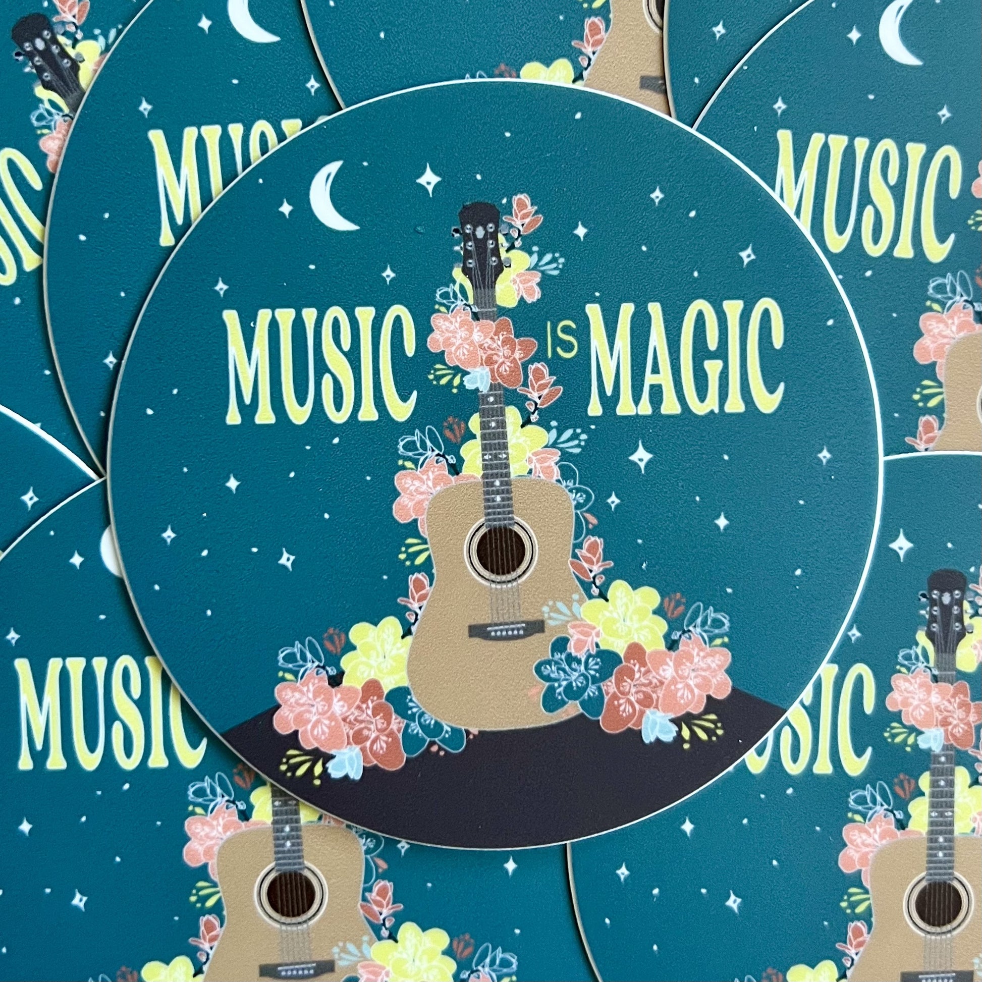 Pile of stickers featurign an illustration of a guitar draped in flowers and the words "music is magic"