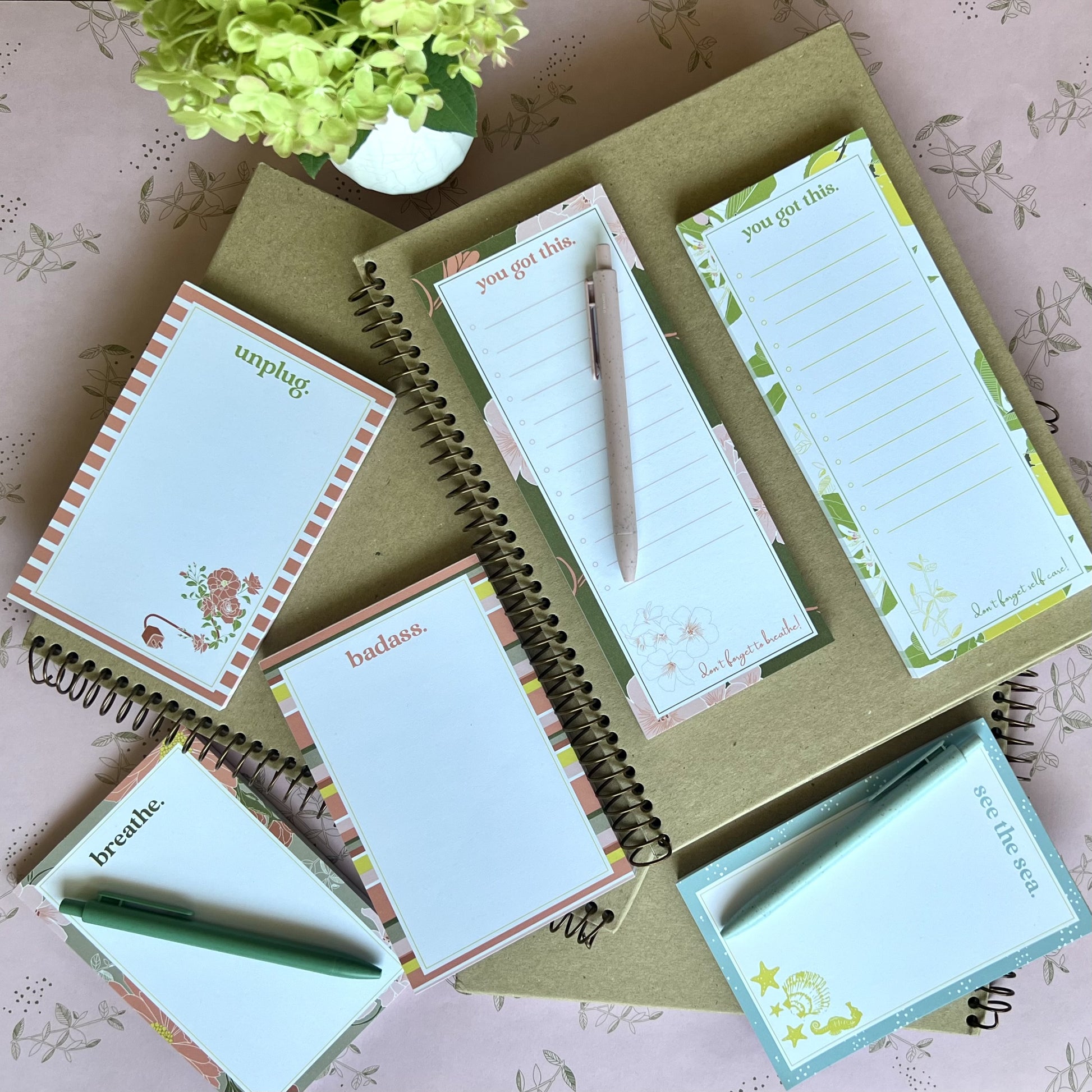 Collection of 6 different notepad styles, stacked on top of kraft paper notebooks with pens & other stationery items