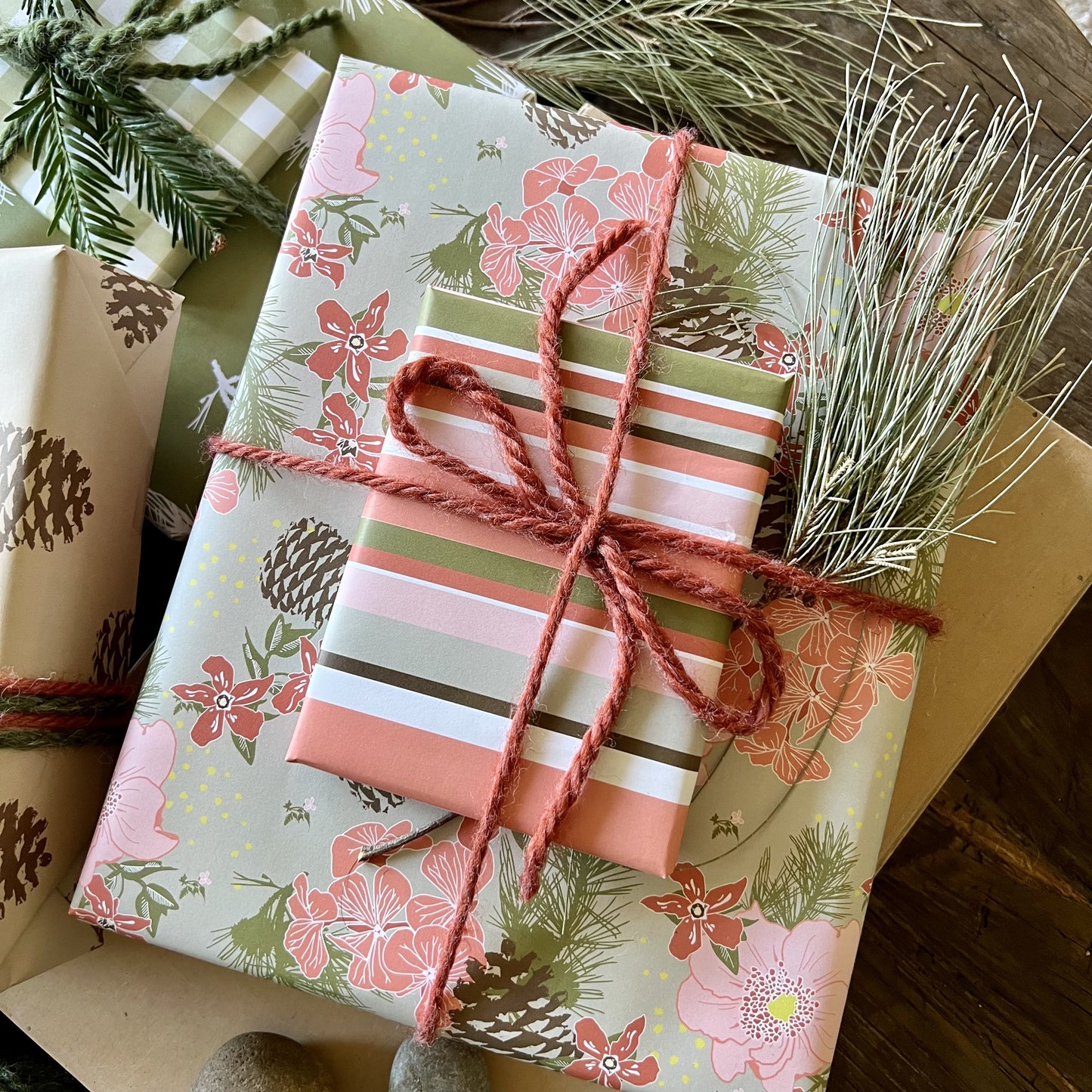 Giftwrapped package with two boxes, one in a pink & olive floral pattern with pinecones, one in a pink & olive stripe