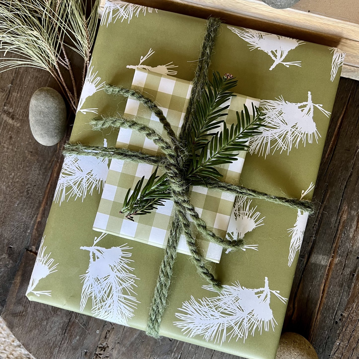 Giftwrapped package with two boxes, one in a green pine branch pattern, one in a green gingham plaid