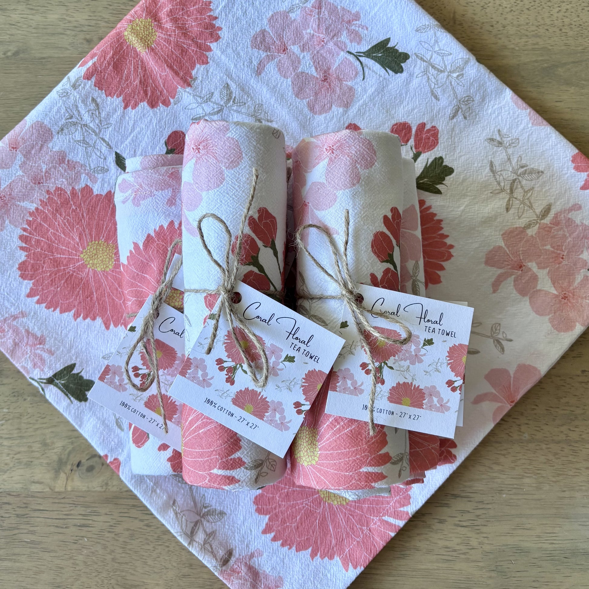 Stack of rolled up pink floral tea towels, tied with twine and square printed hang tags