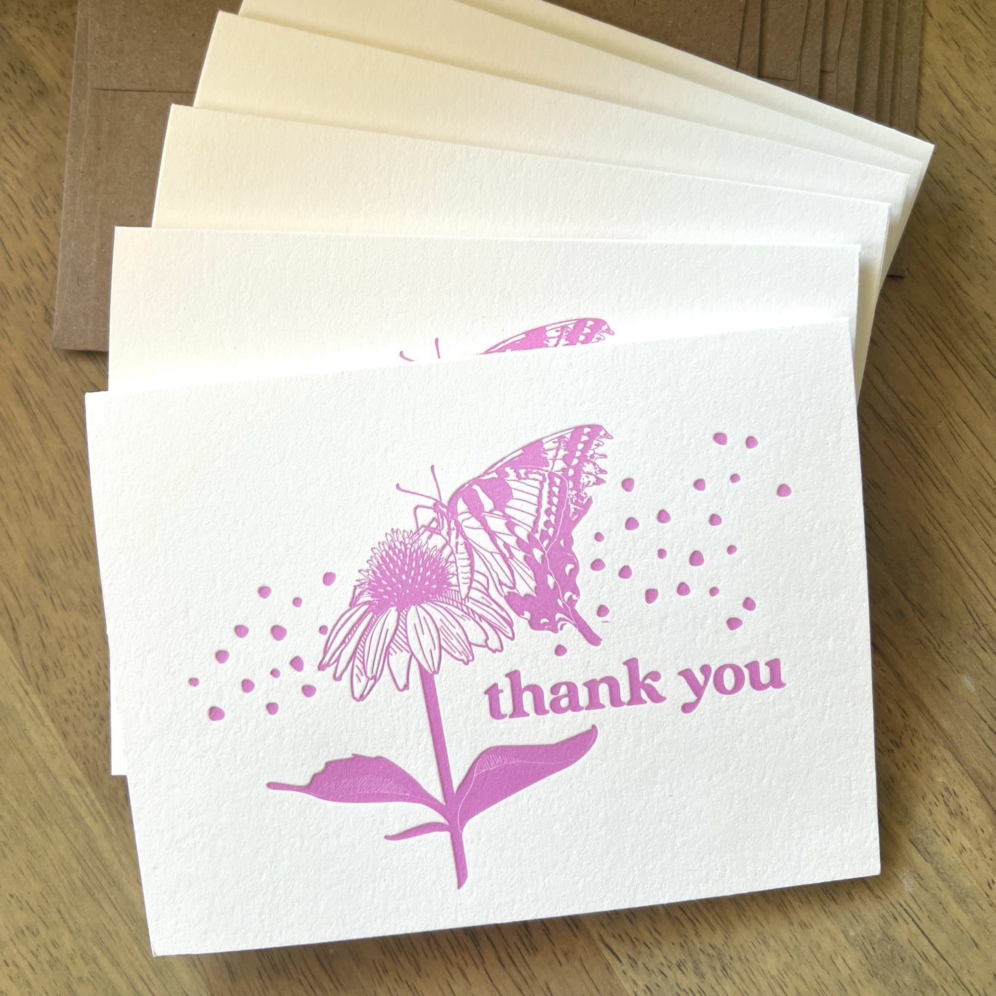 Stack of six letterpress butterfly thank you cards with kraft envelopes on a wooden desk