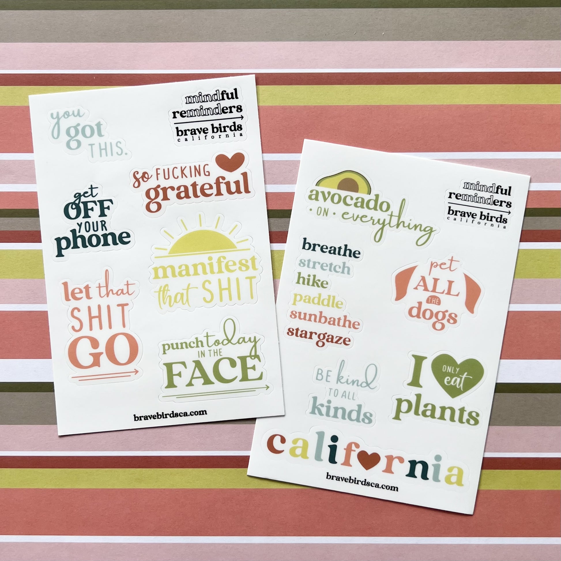 Both versions of sticker sheets, sweary and cali, layed on striped wrapping paper background