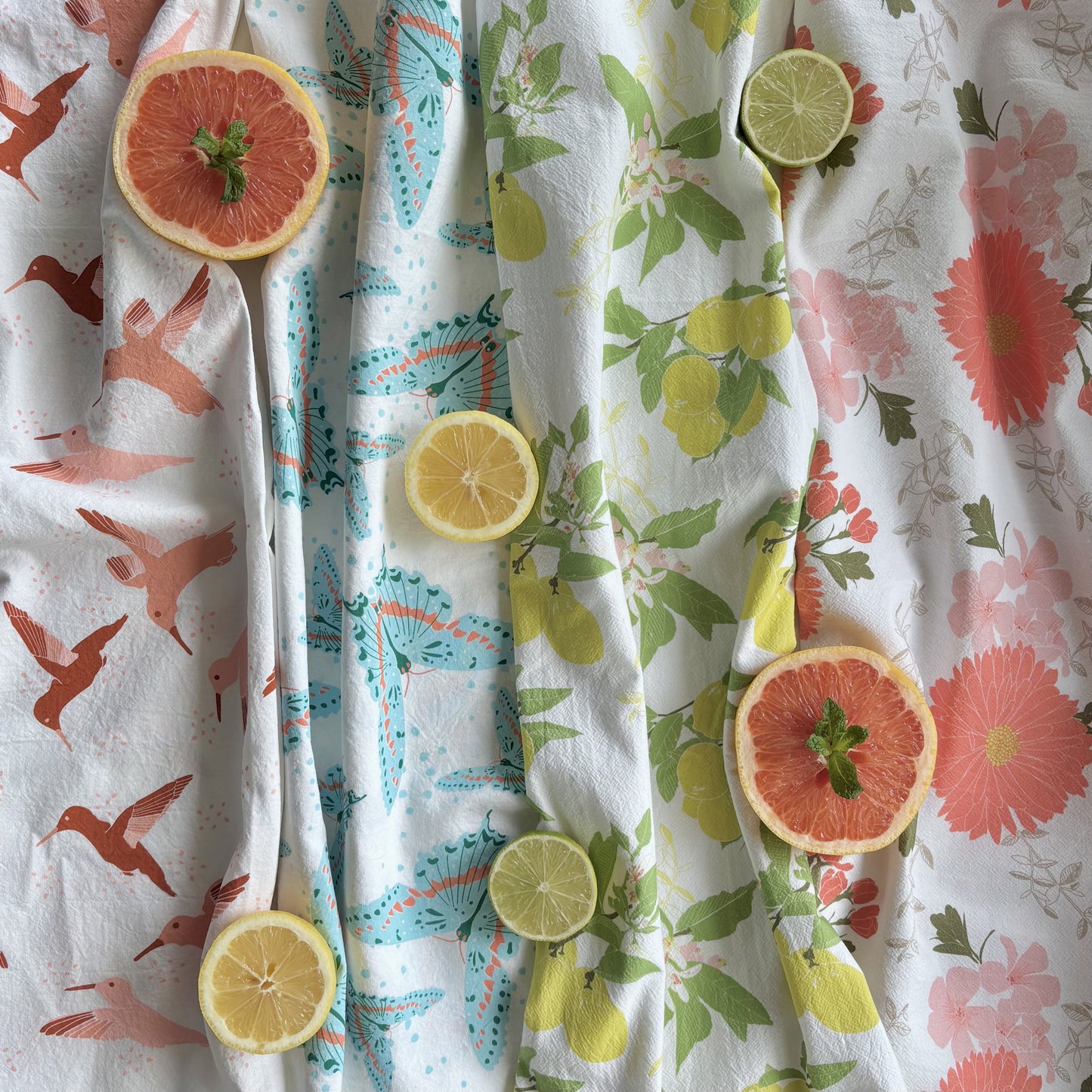 Colorful printed tea towels laid flat and shown with fresh cut citrus fruit halves