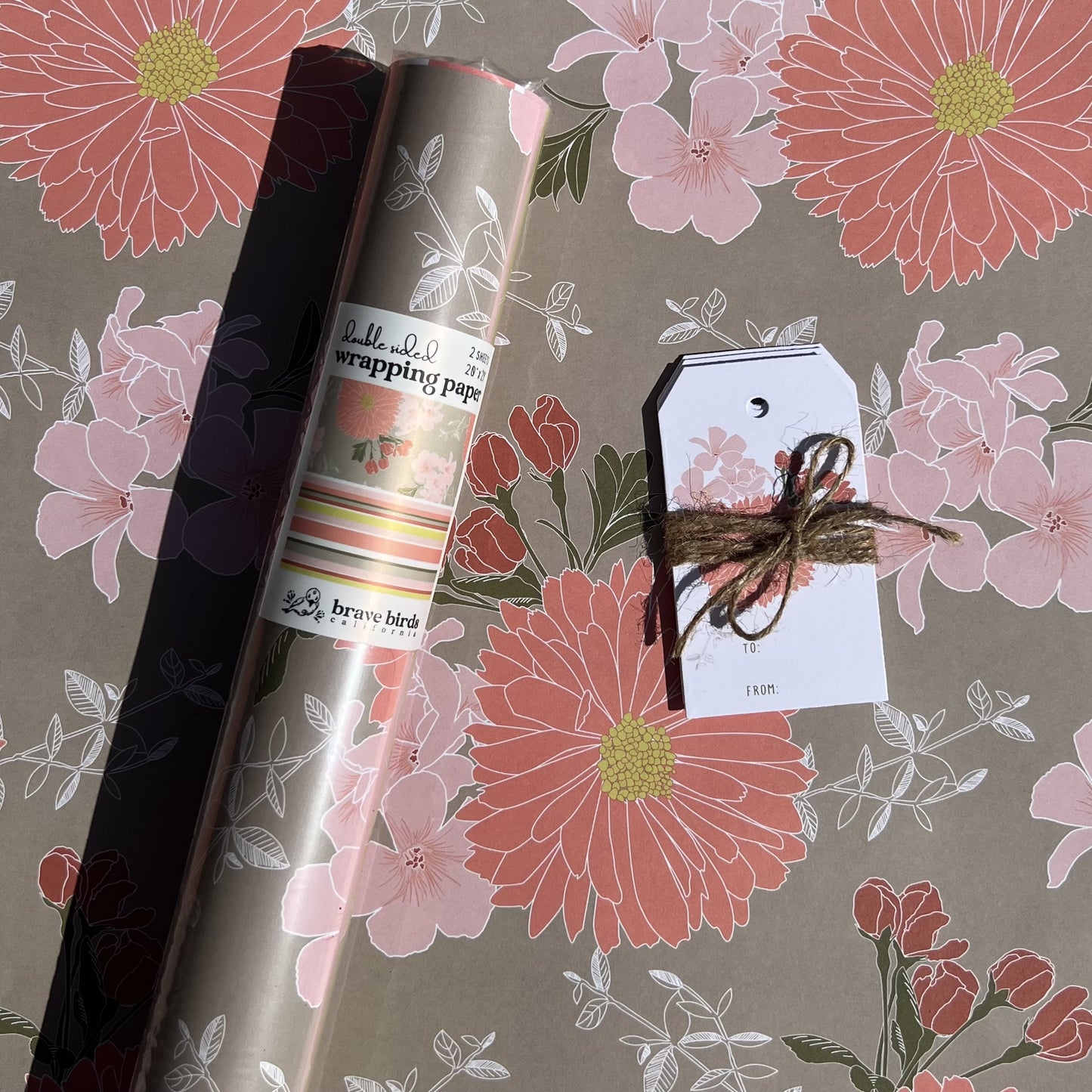 Packaged roll of wrapping paper  sitting on a flat sheet of the paper showing the full pattern, shown with coordinating gift tags
