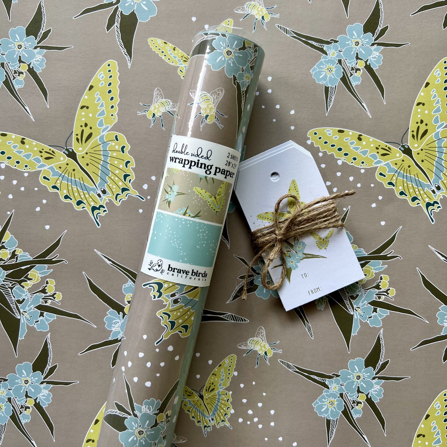Packaged roll of wrapping paper  sitting on a flat sheet of the paper showing the full pattern, shown with coordinating gift tags