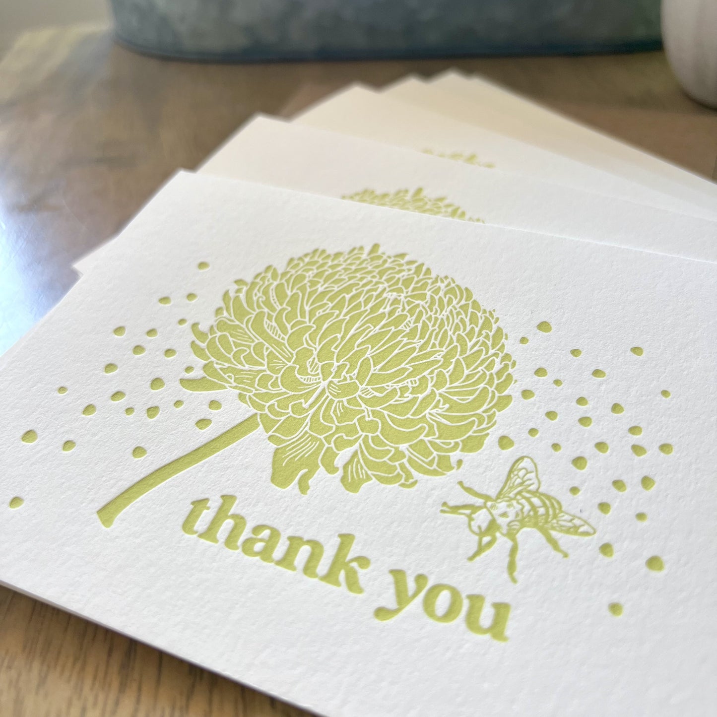 Closeup shot of bee and crysanthemum letterpress thank you cards, with citron yellow ink, showing off the thick texture of the paper and the de-bossed letterpress imprint