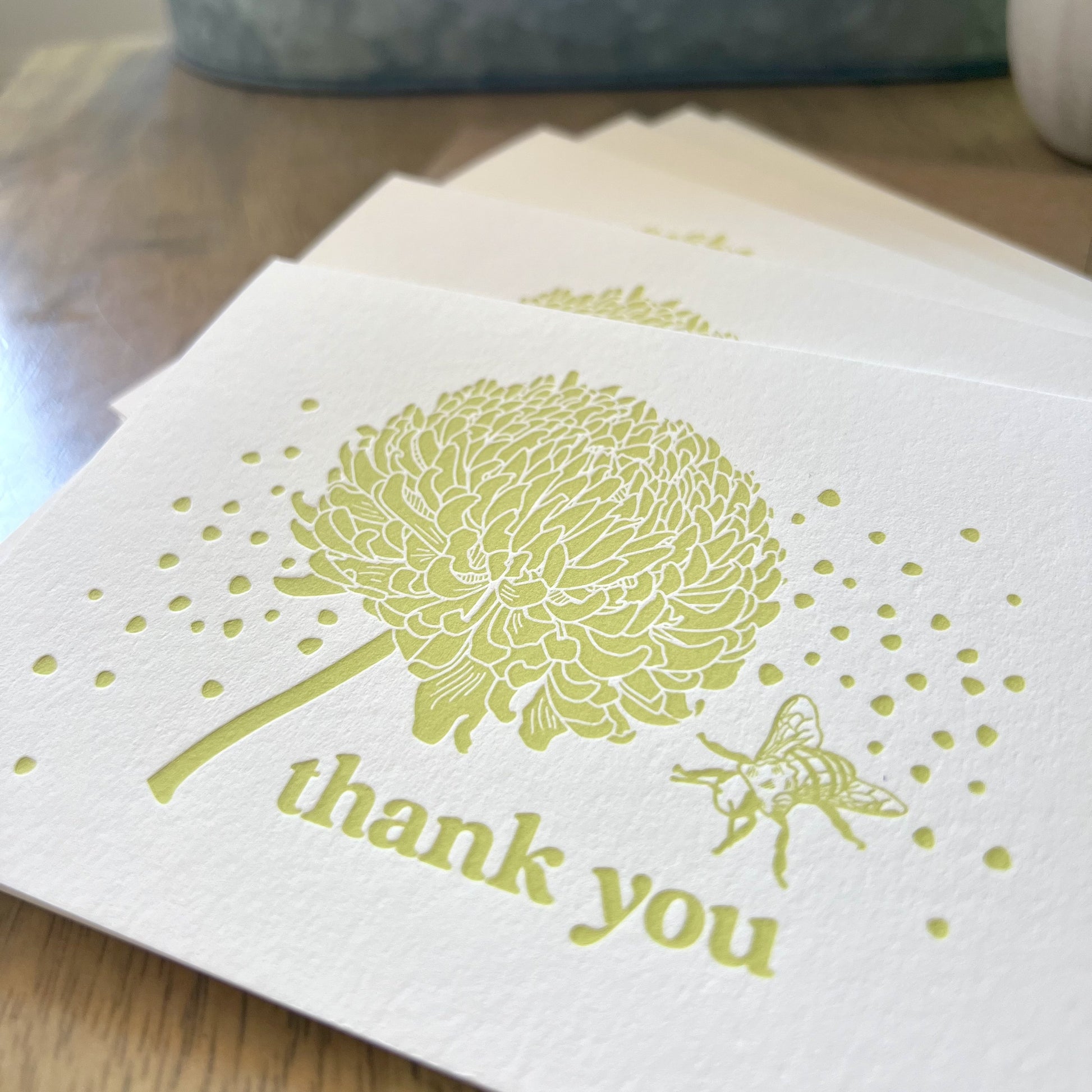 Closeup shot of bee and crysanthemum letterpress thank you cards, with citron yellow ink, showing off the thick texture of the paper and the de-bossed letterpress imprint