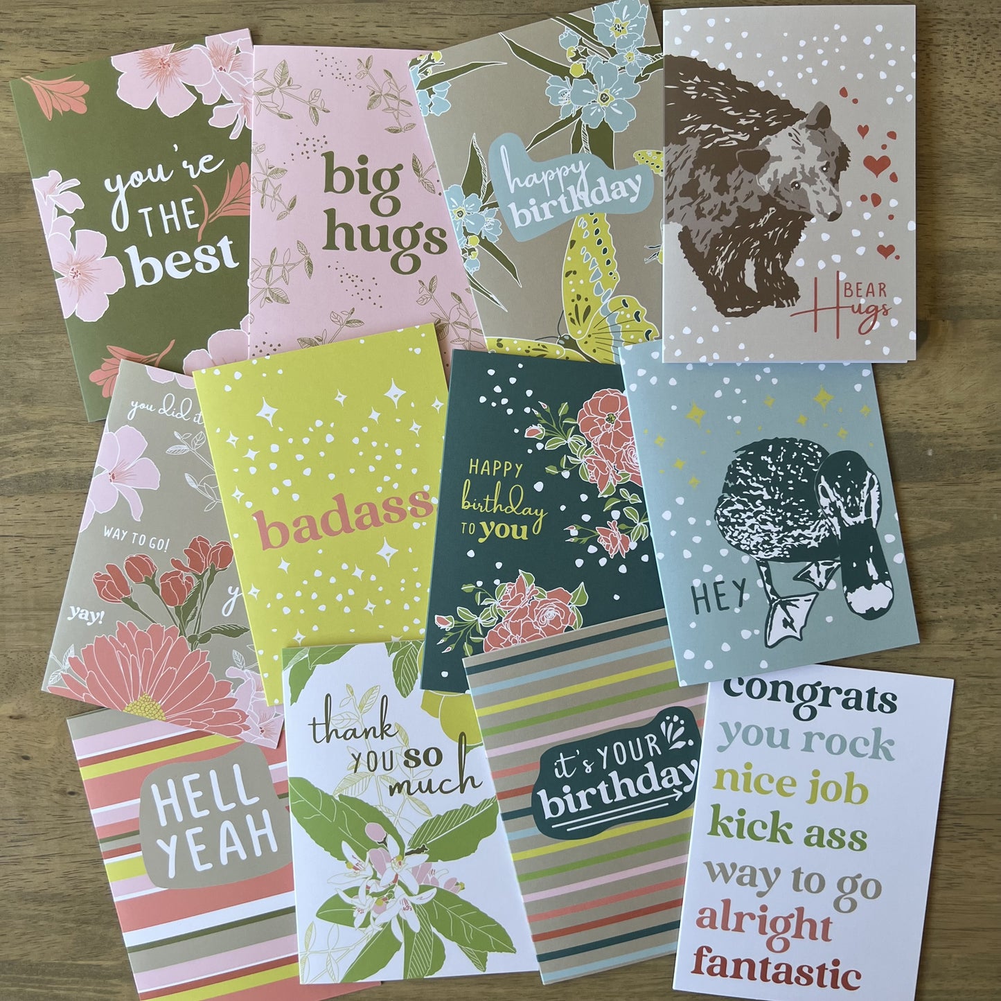 twelve pack of assorted, colorful greeting cards, laid together on a wood table 