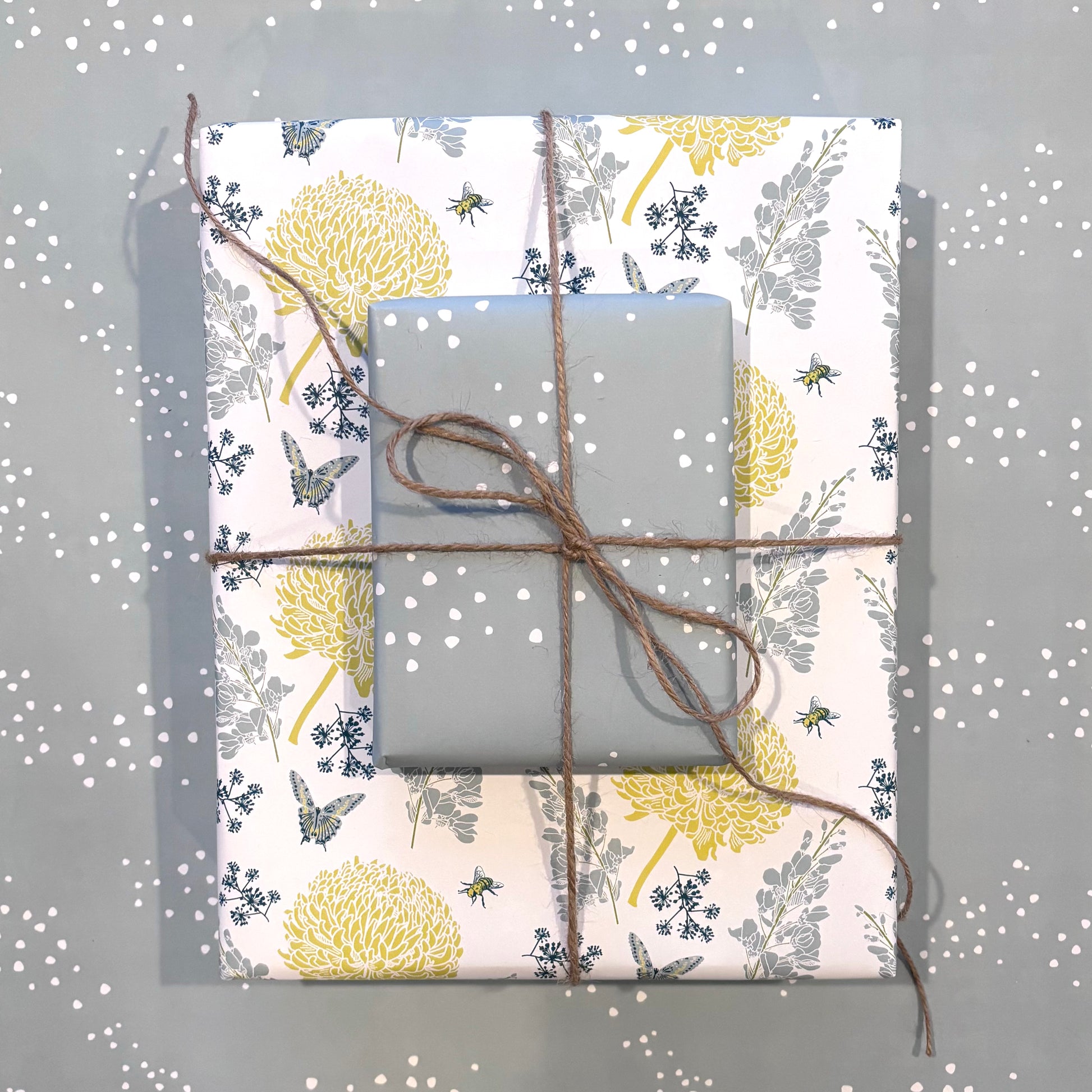 Two gift boxes wrapped in a blue & yellow floral and a blue organic dot pattern, tied with twine