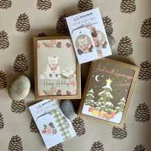 Load image into Gallery viewer, Stack of Holiday stationery. Two boxed card sets and two packs of gift tags. They feature forest illustrations with animals, flowers and a decorated tree.
