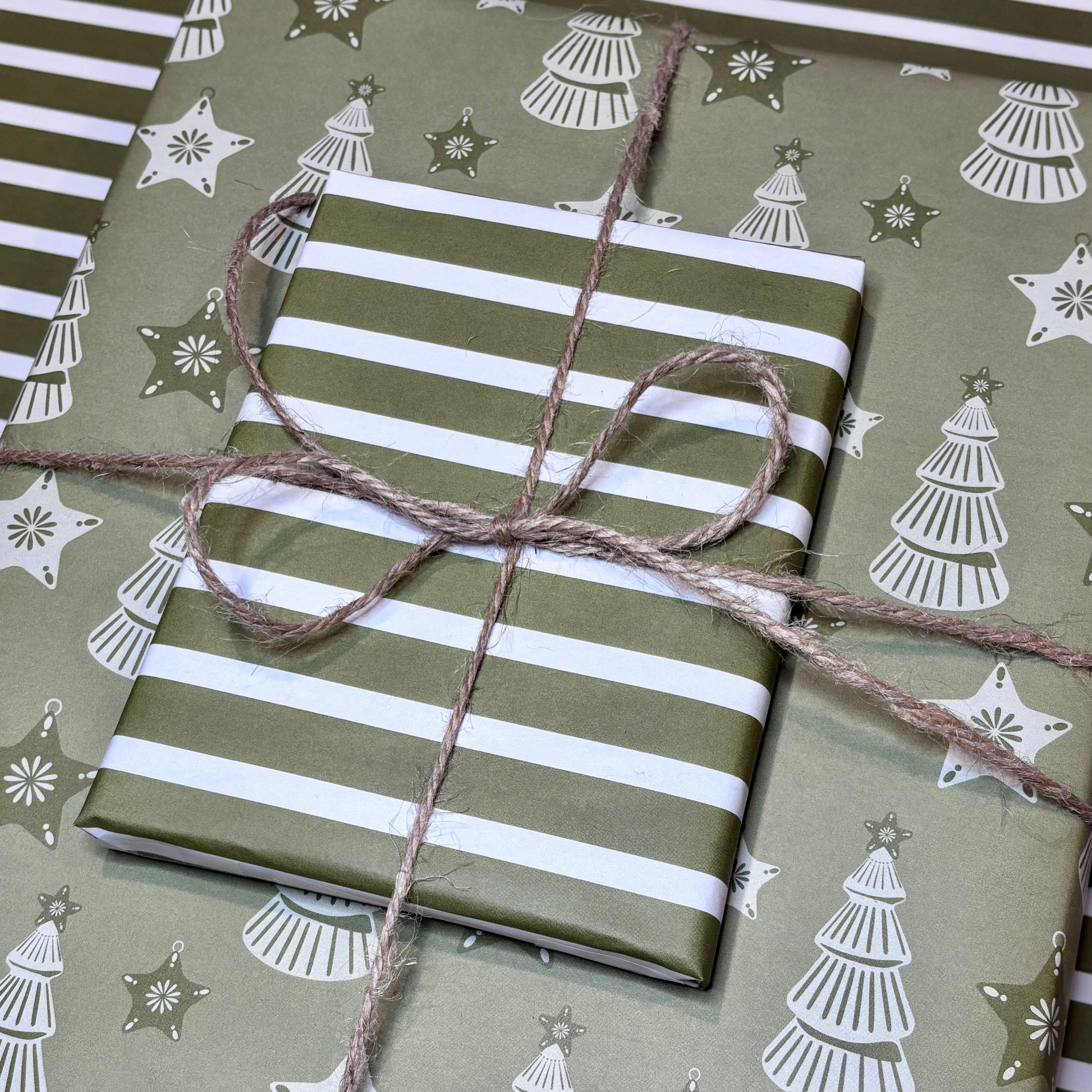 Gift wrapped in green and white striped and Christmas tree paper with twine on a matching background.