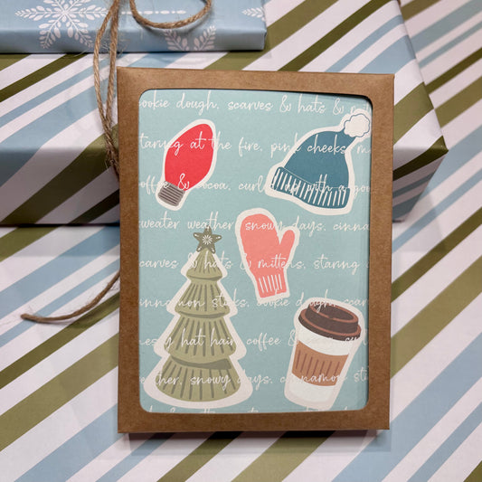 Box of Christmas-themed cards with illustrations of a red light bulb, green tree, pink mittens, and coffee cup on a striped background.