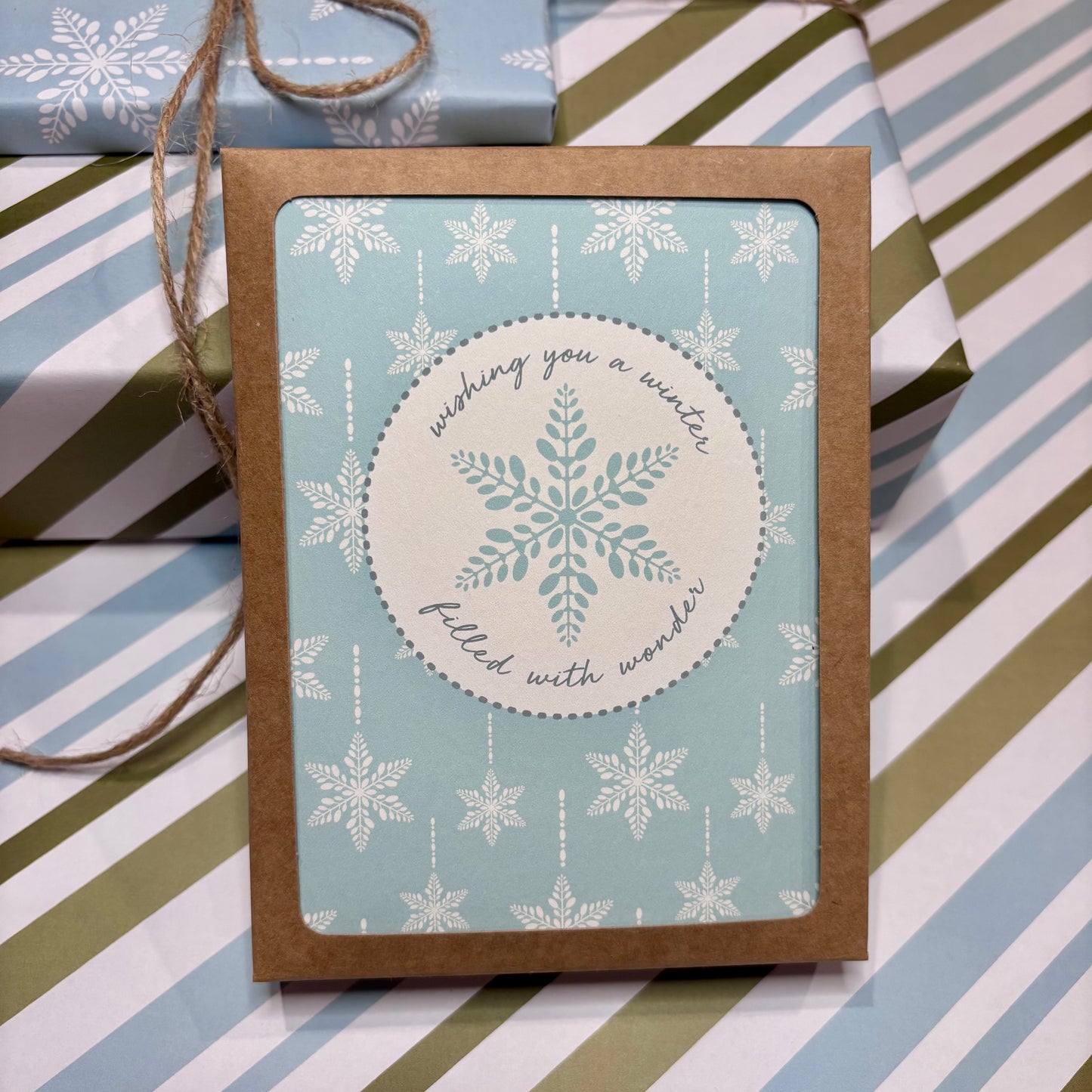 Greeting card with snowflake design and script text that says 'wishing you a winter filled with wonder' on a striped background