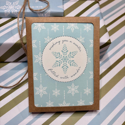 Greeting card with snowflake design and script text that says 'wishing you a winter filled with wonder' on a striped background