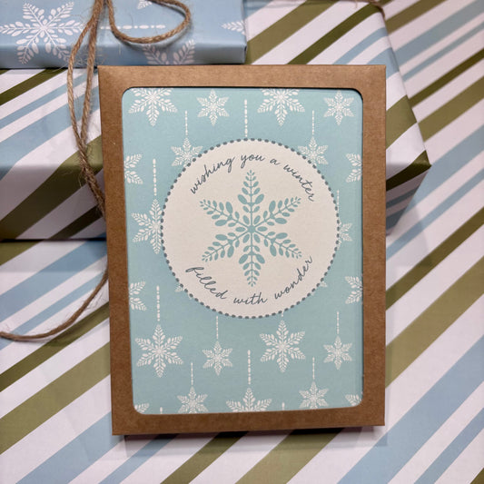 Greeting card with snowflake design and script text that says 'wishing you a winter filled with wonder' on a striped background