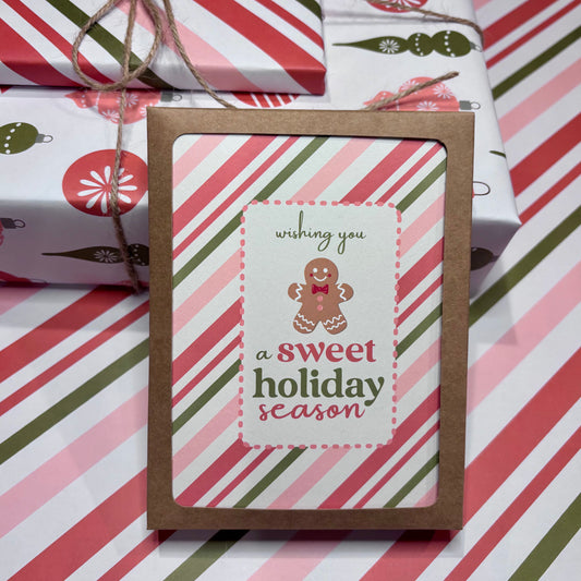 Greeting card with 'wishing you a sweet holiday season' text and gingerbread man on striped gift wrap background
