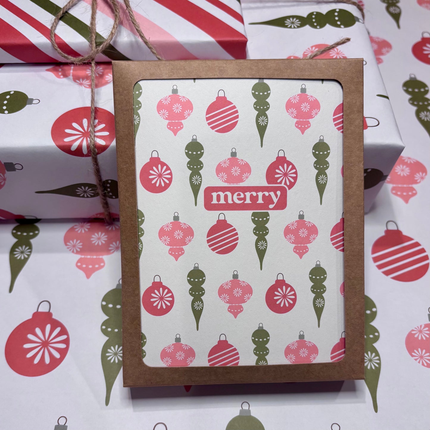 Card with Christmas ornament pattern and 'merry' text, surrounded by wrapped gifts.