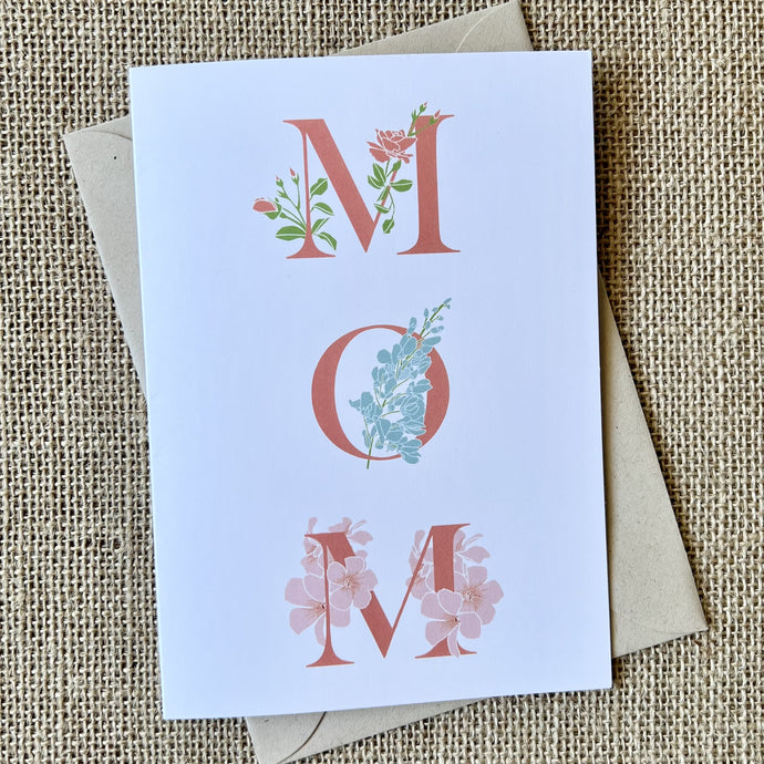 Greeting card with capital letters M-O-M in dark pink and flower illustrations wrapping around the letters