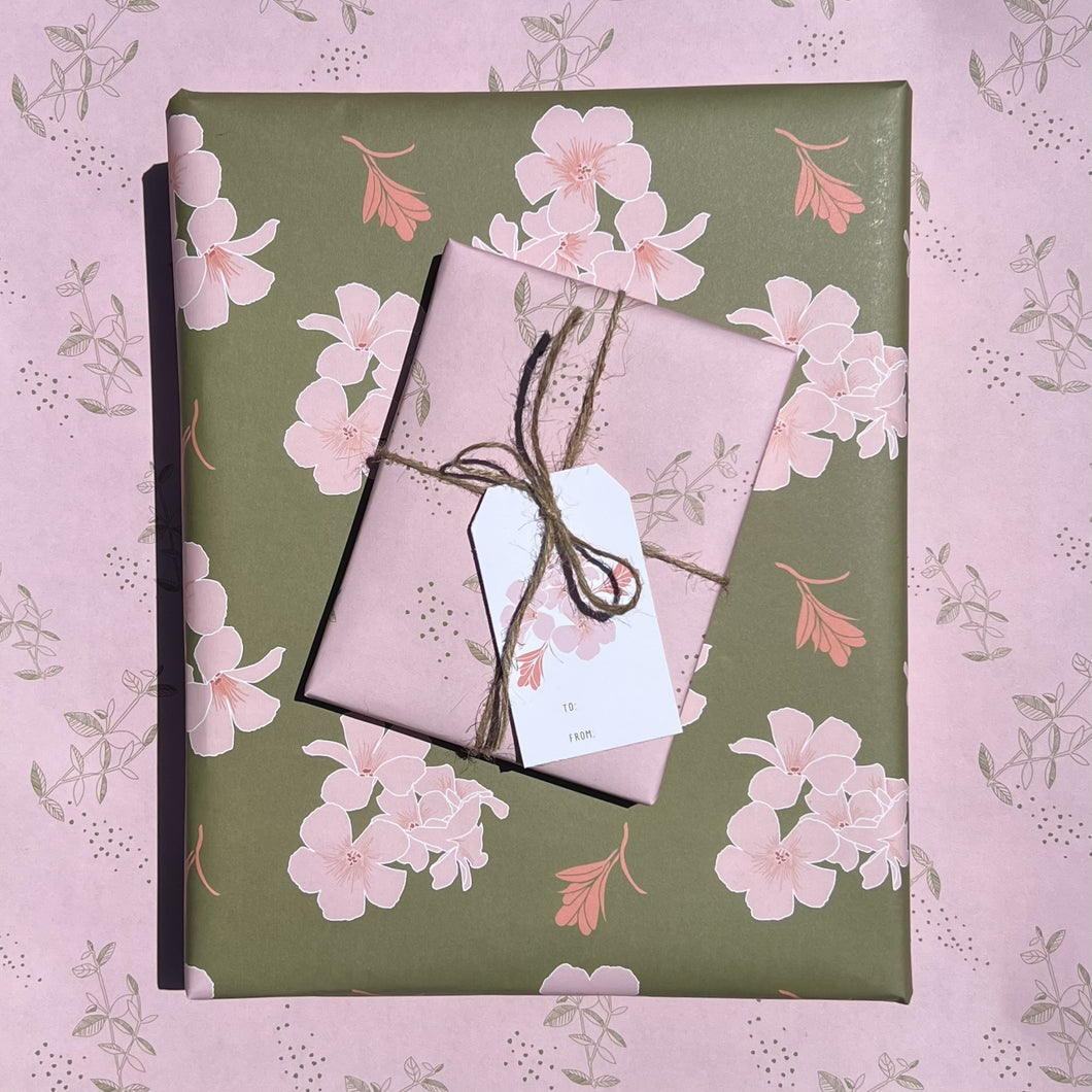 Two gift boxes, one wrapped in olive ground print, one wrapped in light pink print, tied with twine, and topped with a pink blossom gift tag