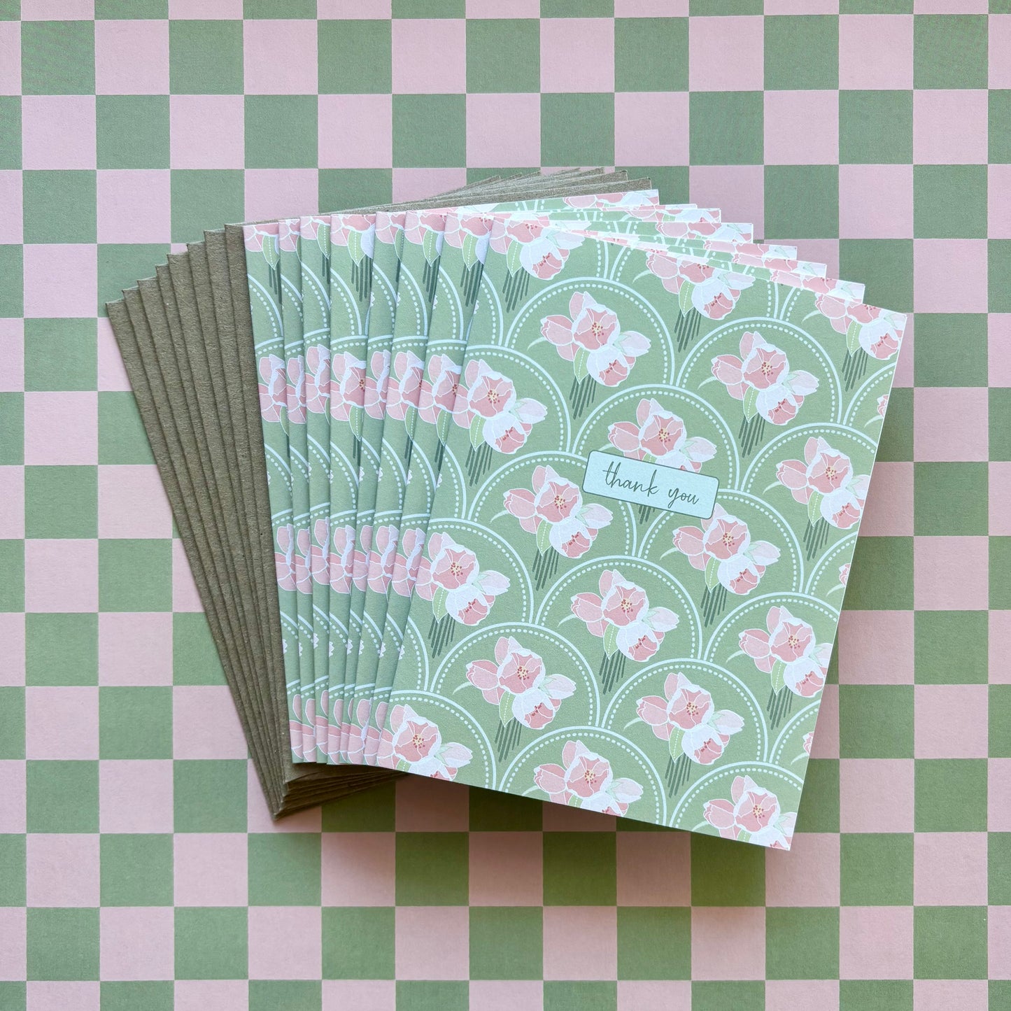 Fanned stack of eight thank you greeting cards with pink flowers on a green scallop pattern background and kraft brown envelopes