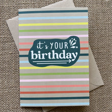 Load image into Gallery viewer, Rainbow striped background with a teal organic shape, saying &quot;It&#39;s your birthday&quot; in white type, show with kraft paper envelope
