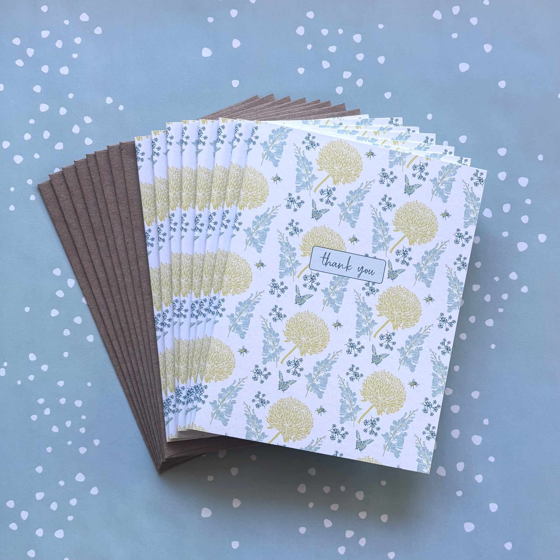 Fanned stack of eight thank you greeting cards with yellow & blue floral print, and kraft brown envelopes