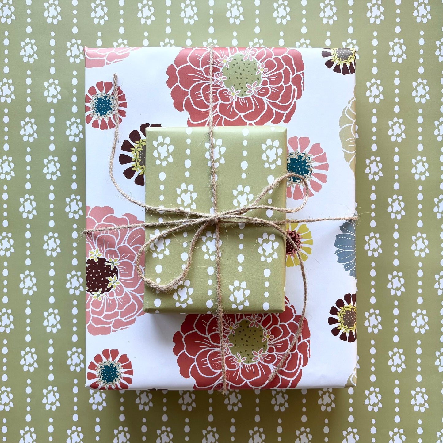 Two gift boxes , one with a colorful floral patten on a cream background and the other with a green grounded organic dot print, tied with twine