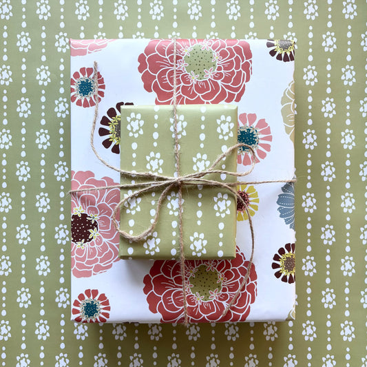Two gift boxes , one with a colorful floral patten on a cream background and the other with a green grounded organic dot print, tied with twine