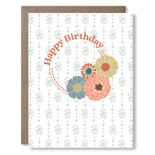 Greeting card with light blue dot-stripe background and a circular lockup of zinnia flowers and text reading "Happy Birthday"