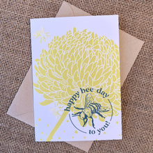 Load image into Gallery viewer, Greeting card with white background, citron chrysanthemum flower and teal bee illustration and text reading &quot;happy bee-day to you&quot;, styled with a kraft envelope on a tan burlap background
